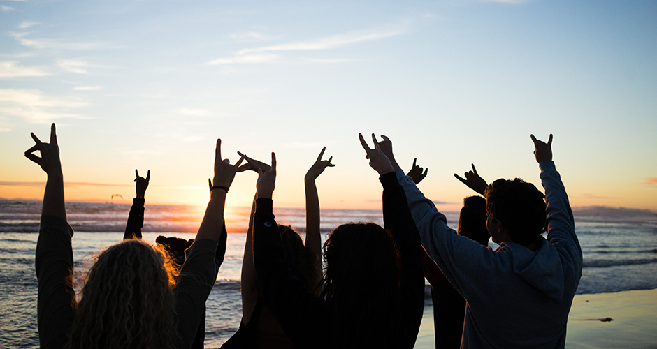 students at a beach during sunset doing the zot sign